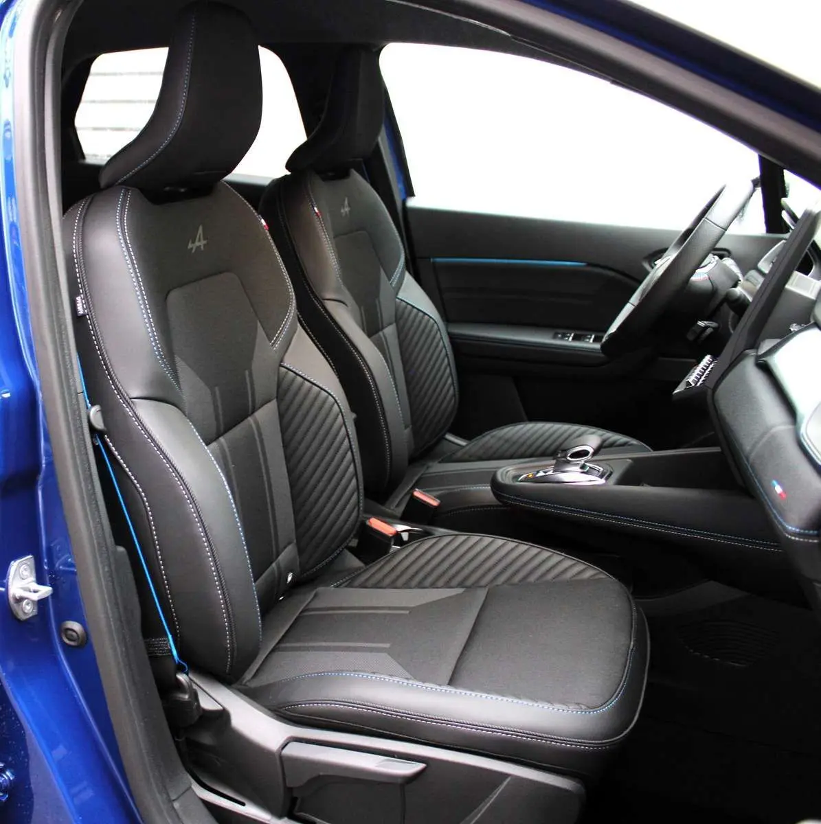 Intérieur côté conducteur du Renault Captur 2025 bleu iron metal, sièges noirs avec surpiqûres bleues et logo Alpine brodé.