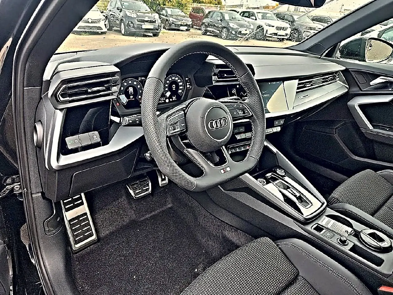Vue intérieure côté conducteur de l’Audi A3 Sportback noir mythos, volant sport et tableau de bord digital visible.