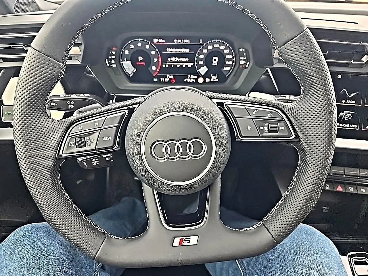 Vue intérieure centrée sur le volant sport en cuir noir avec logo S et tableau de bord numérique d'une Audi A3 Sportback.