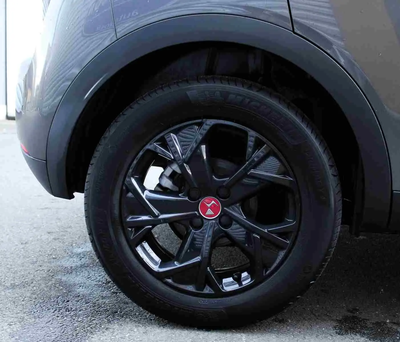 Gros plan sur la roue arrière droite du DS3 Crossback gris platinium métal, jante noire brillante avec logo rouge au centre.