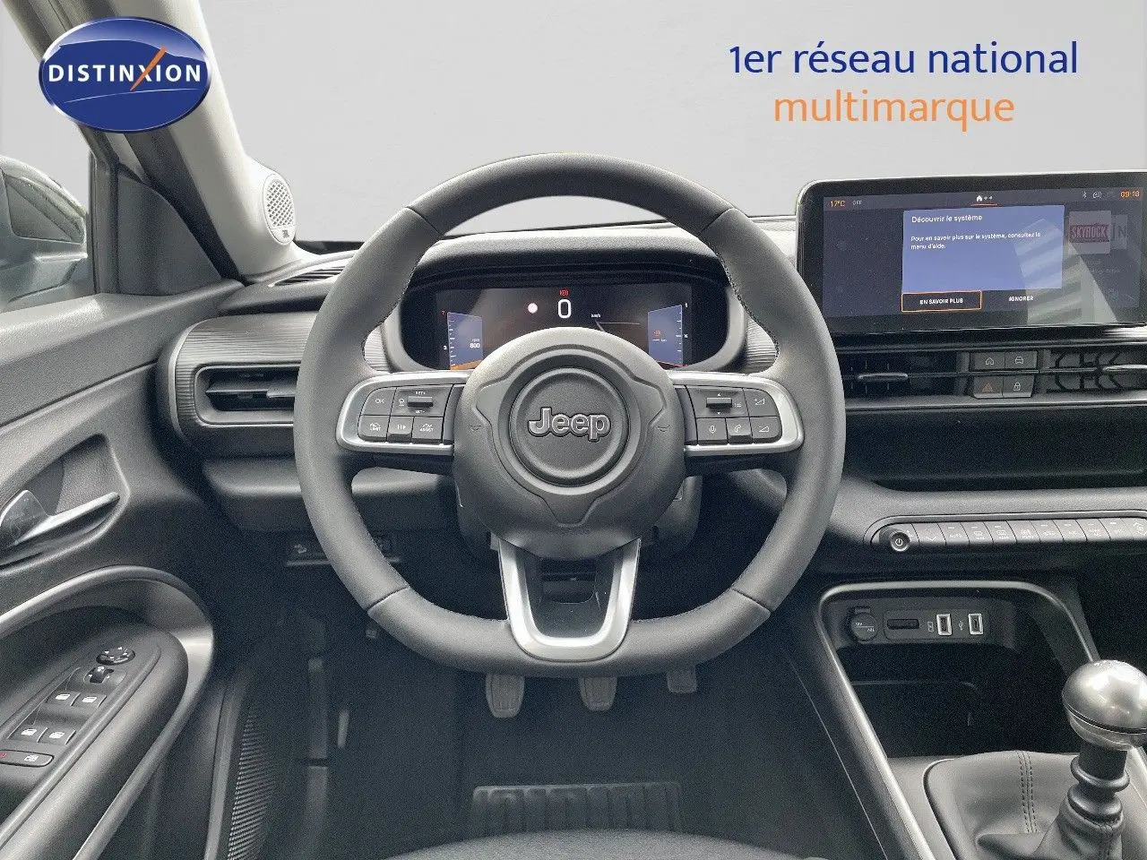 Intérieur du Jeep Avenger 2024 blanc neige, vue frontale sur le volant, tableau de bord numérique et levier de vitesse manuel.