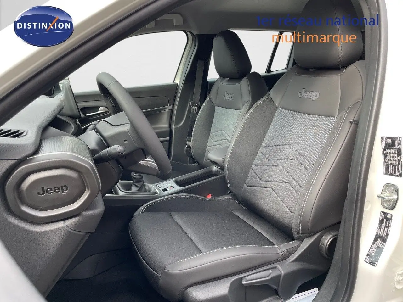 Vue intérieure côté conducteur du Jeep Avenger blanc neige 2024, sièges noirs en cuir et tissu avec logo Jeep brodé.