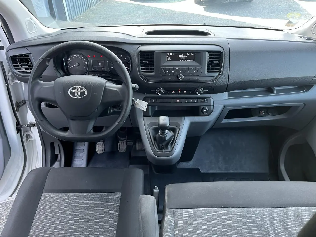 Vue intérieure avant du Toyota Proace Fourgon blanc 2021, tableau de bord avec volant, boîte manuelle et écran central simple.