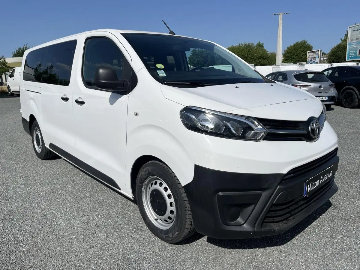 Vue 3/4 avant d'un Toyota Proace Fourgon blanc avec pare-chocs noirs et jantes acier 16 pouces sur parking.