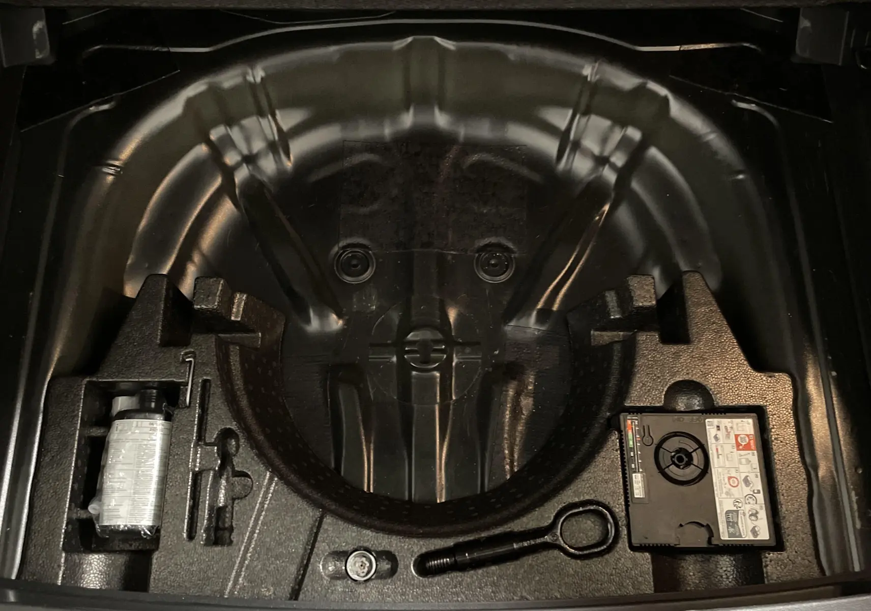 Compartiment de rangement sous coffre noir du Volkswagen T-Roc 2024 avec kit de réparation pneus intégré.