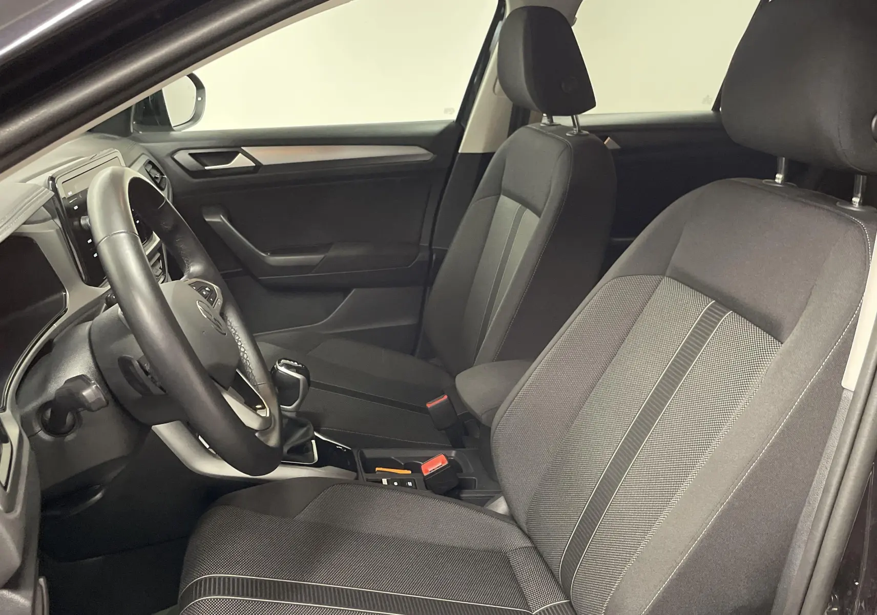 Intérieur côté conducteur du Volkswagen T-Roc 2024 noir, montrant sièges tissu et tableau de bord moderne.