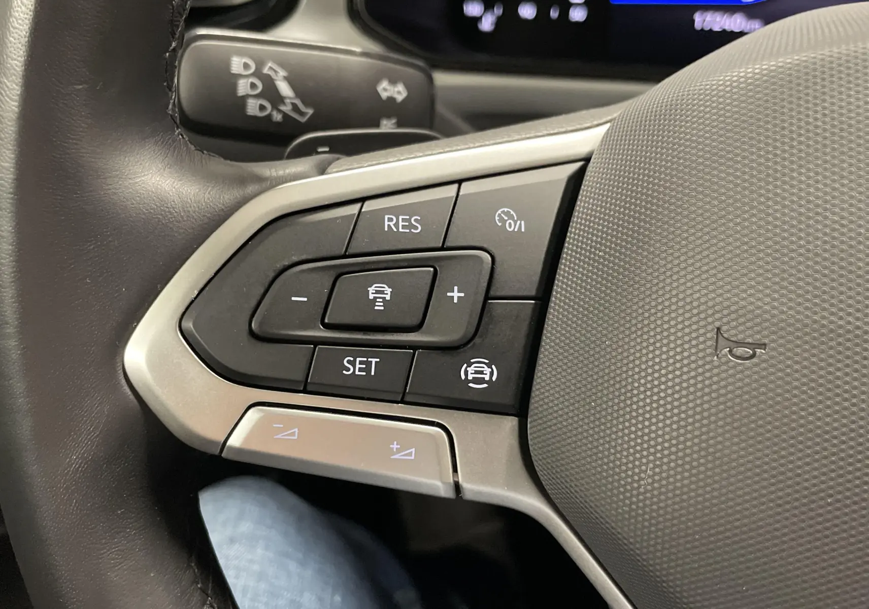 Gros plan sur les commandes du régulateur de vitesse au volant d'un Volkswagen T-Roc 2024 noir intense nacré.