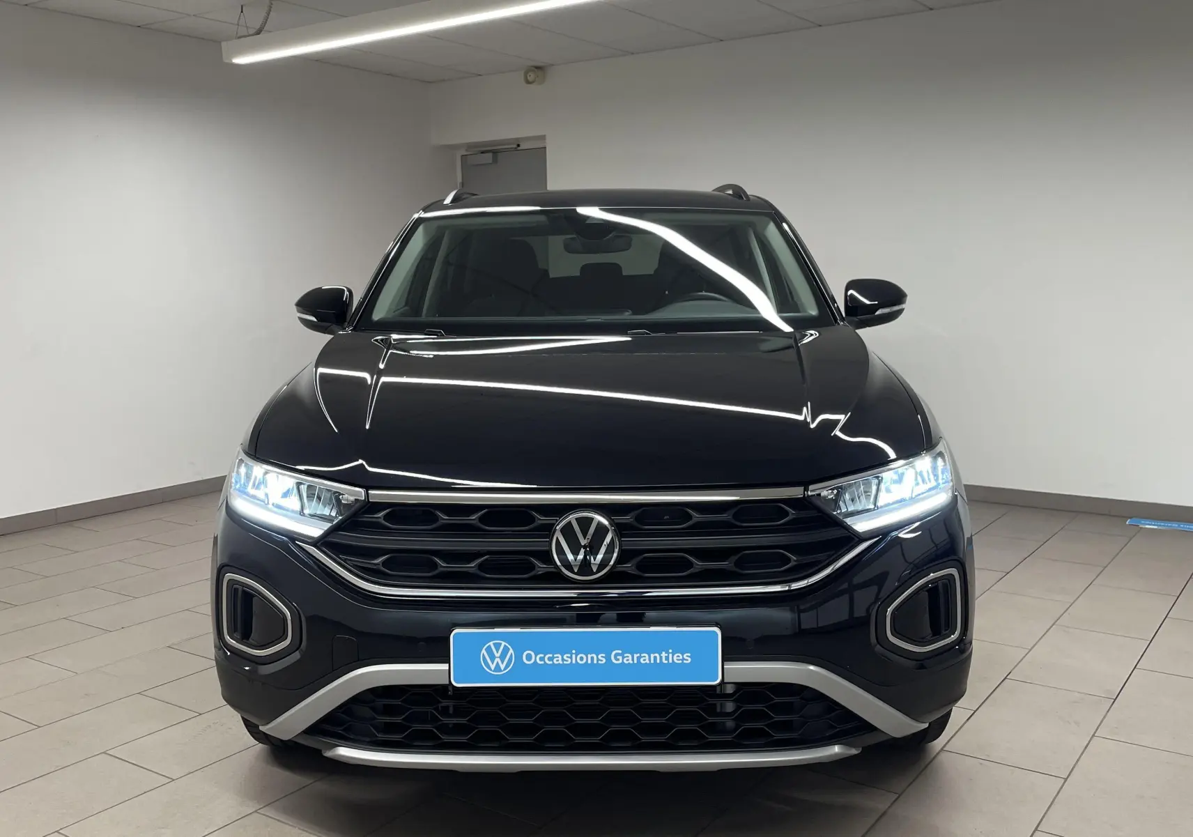 Vue frontale d'un Volkswagen T-Roc 1.5 TSI 150 DSG7 noir intense nacré avec phares LED allumés en intérieur.