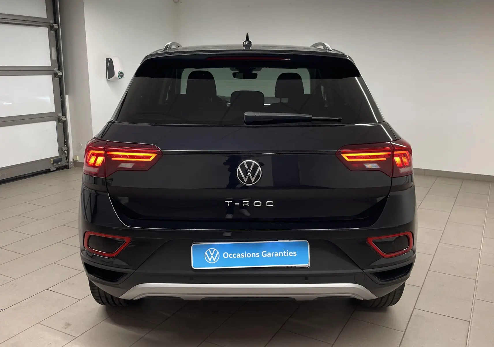 Vue arrière d'un Volkswagen T-Roc 2024 noir intense nacré avec feux allumés et plaque "Occasions Garantis".