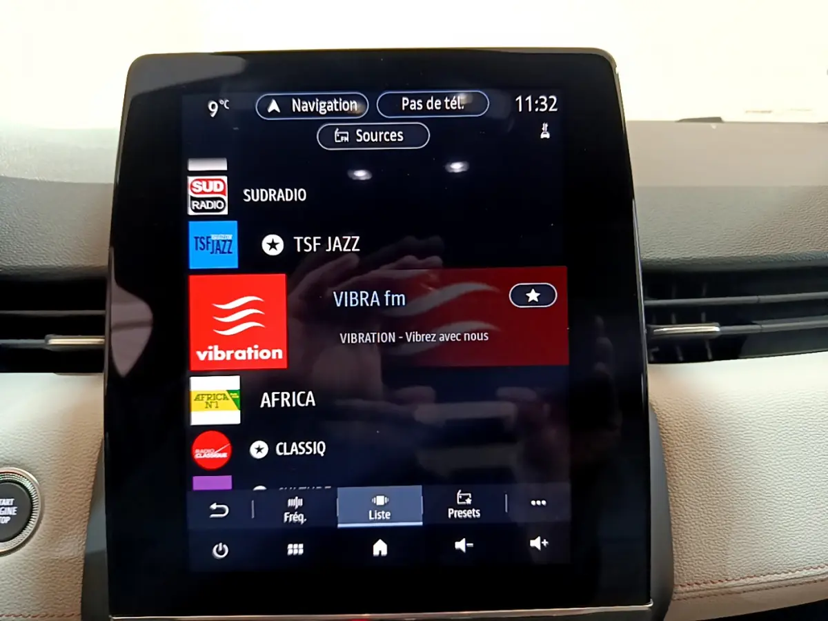 Écran tactile central affichant les stations radio dans l'habitacle clair de la Renault Clio Initiale Paris orange.