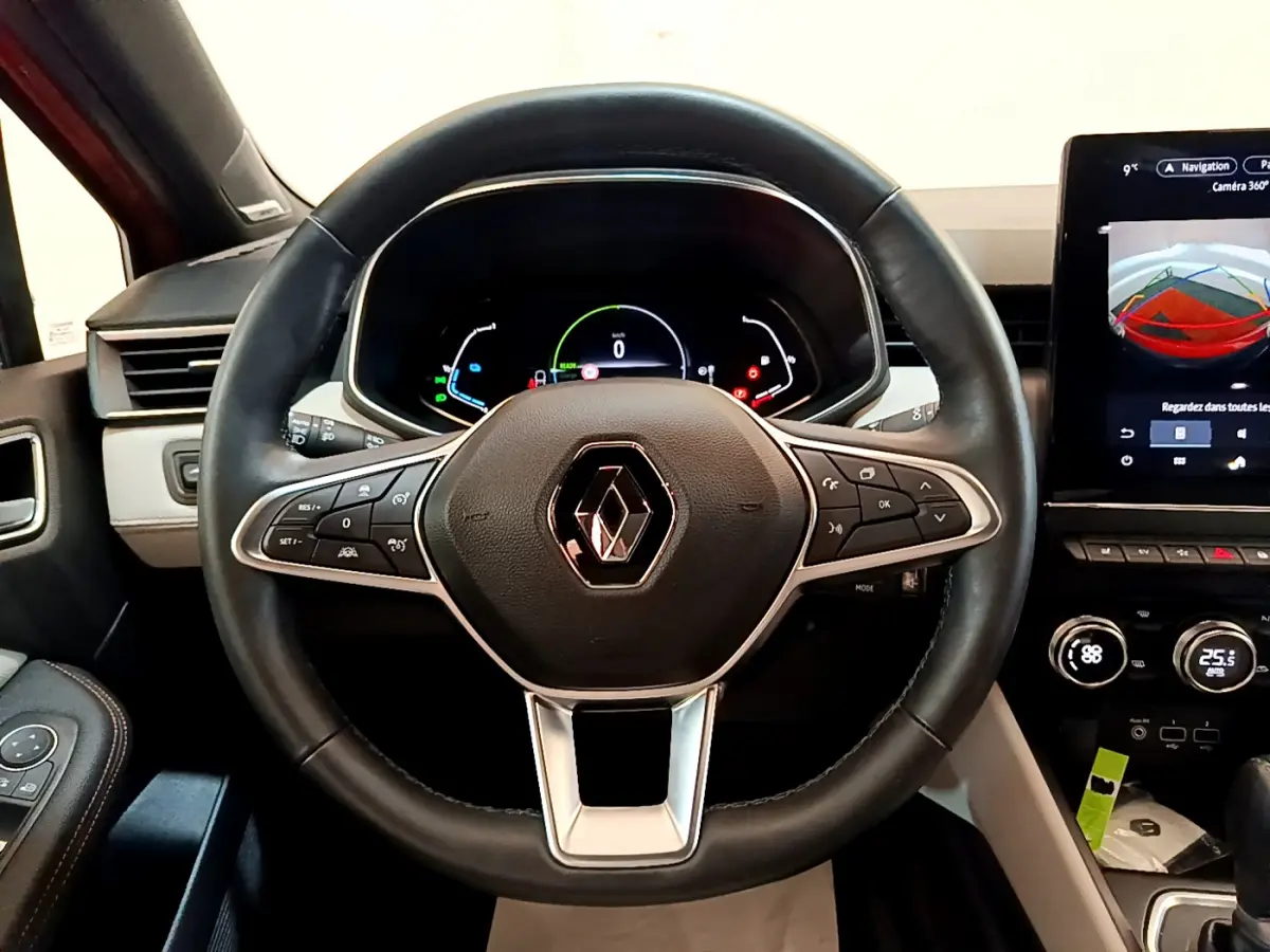 Volant cuir noir avec logo Renault au centre, tableau de bord numérique et écran tactile affichant la caméra 360° dans une Renault Clio orange.