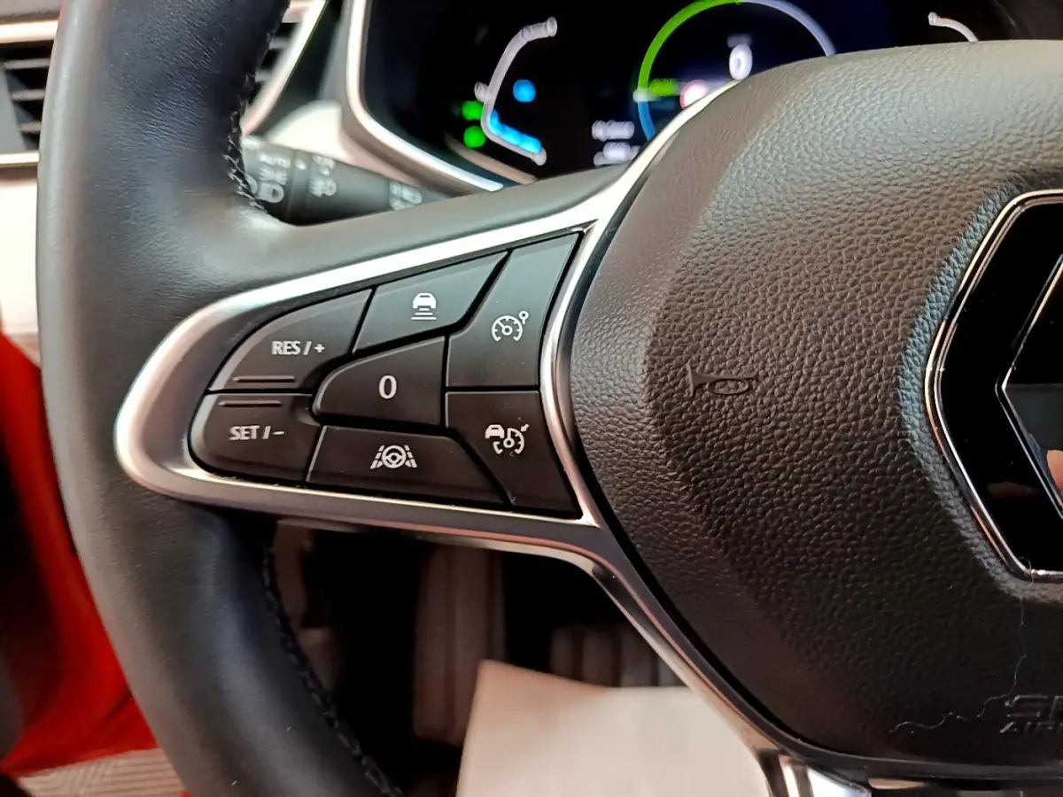 Gros plan sur le volant noir de la Renault Clio Initiale Paris orange, avec commandes de régulateur de vitesse visibles à gauche.