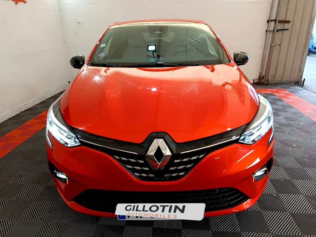 Vue avant d'une Renault Clio Initiale Paris E-TECH 140 orange avec phares LED allumés dans un garage.