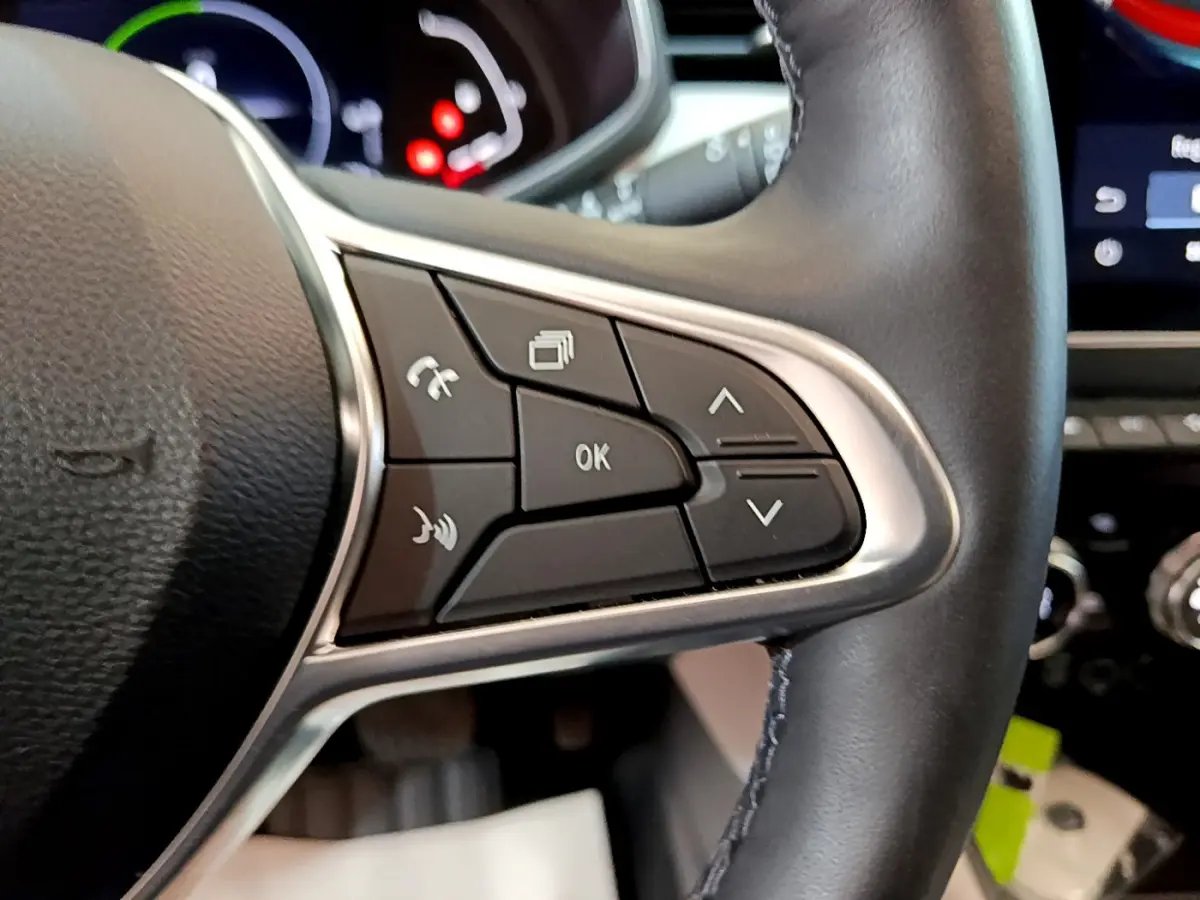 Gros plan sur les commandes du volant droit en cuir noir de la Renault Clio Initiale Paris orange, avec écran tactile en arrière-plan.