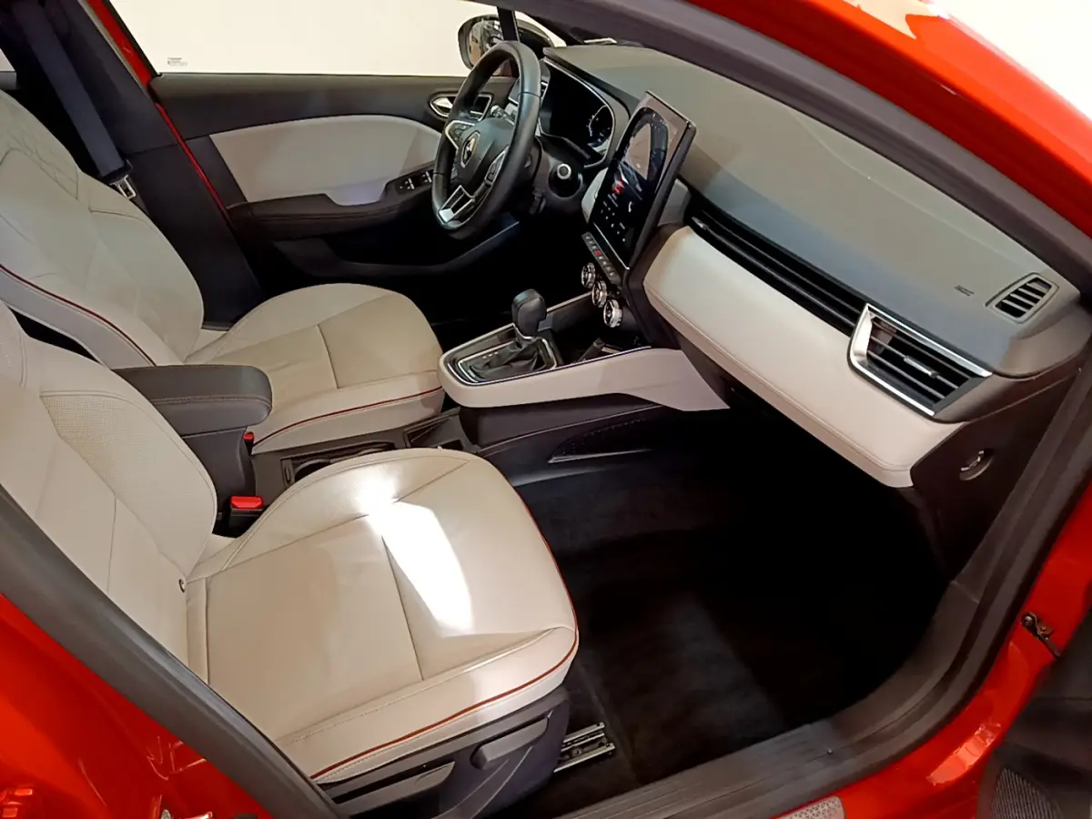 Intérieur côté conducteur d'une Renault Clio orange 2021, sièges clairs et tableau de bord avec écran tactile vertical.