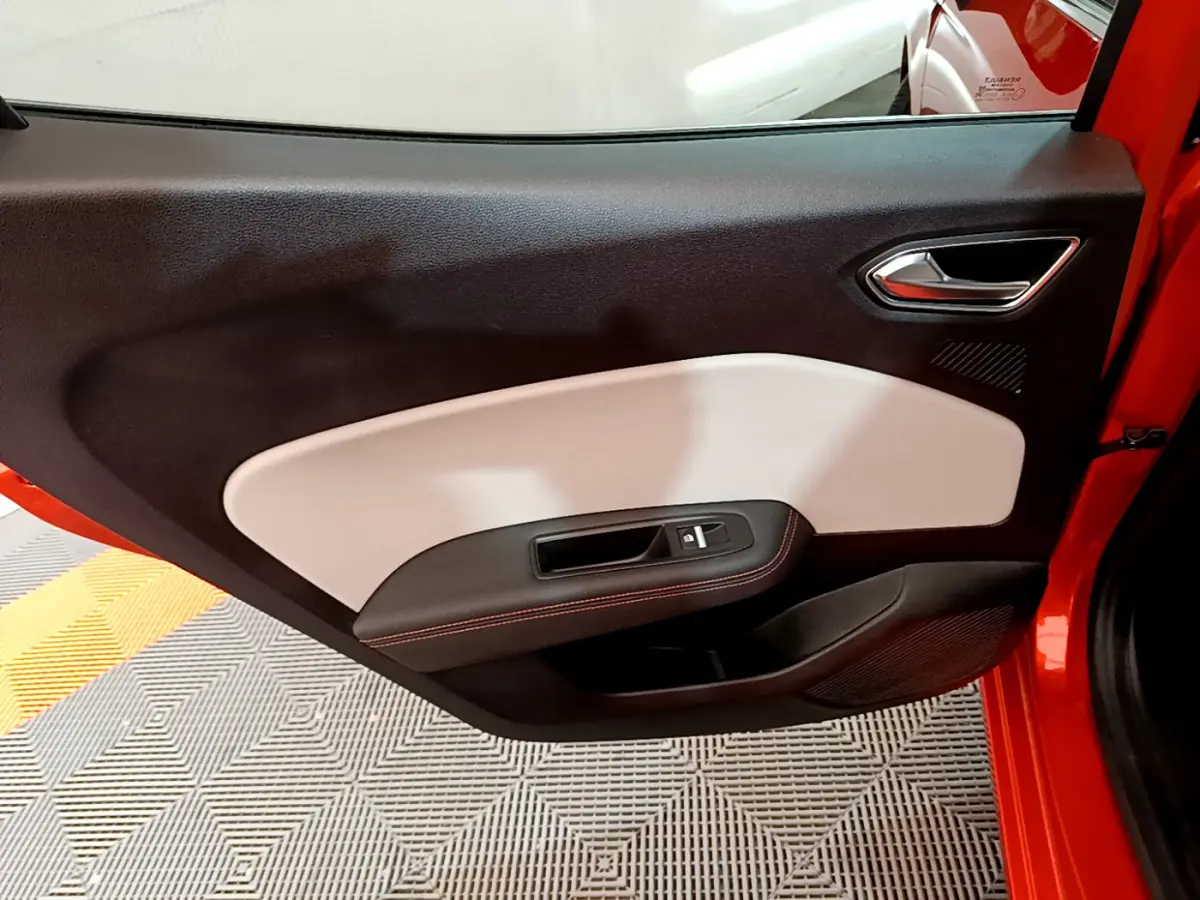 Porte côté gauche ouverte de la Renault Clio Initiale Paris orange, intérieur noir et beige avec surpiqûres rouges.