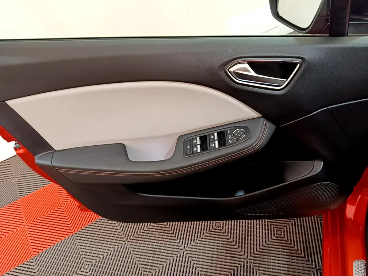 Vue intérieure du panneau de porte avant gauche de la Renault Clio orange, avec commandes électriques et poignée chromée.