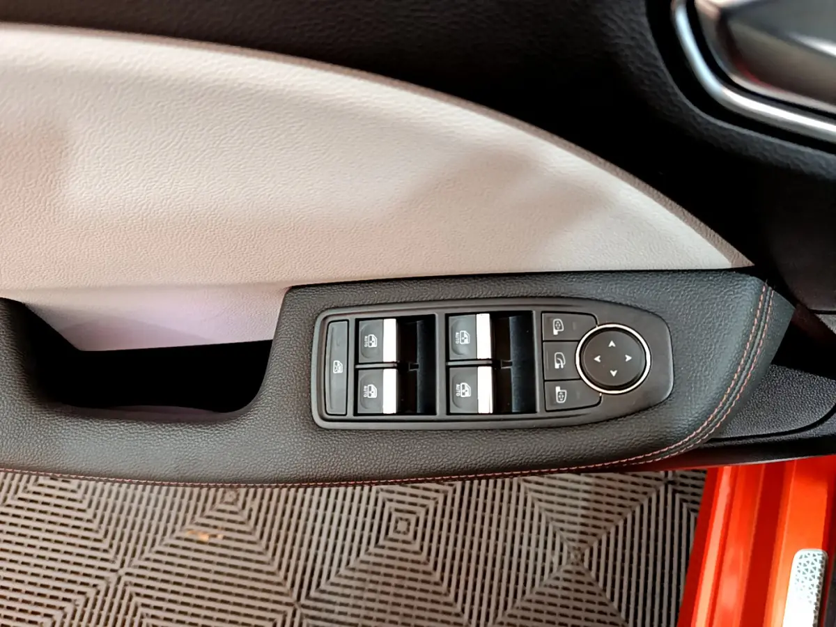 Gros plan sur la commande des vitres côté conducteur de la Renault Clio Initiale Paris orange, avec surpiqûres rouges.