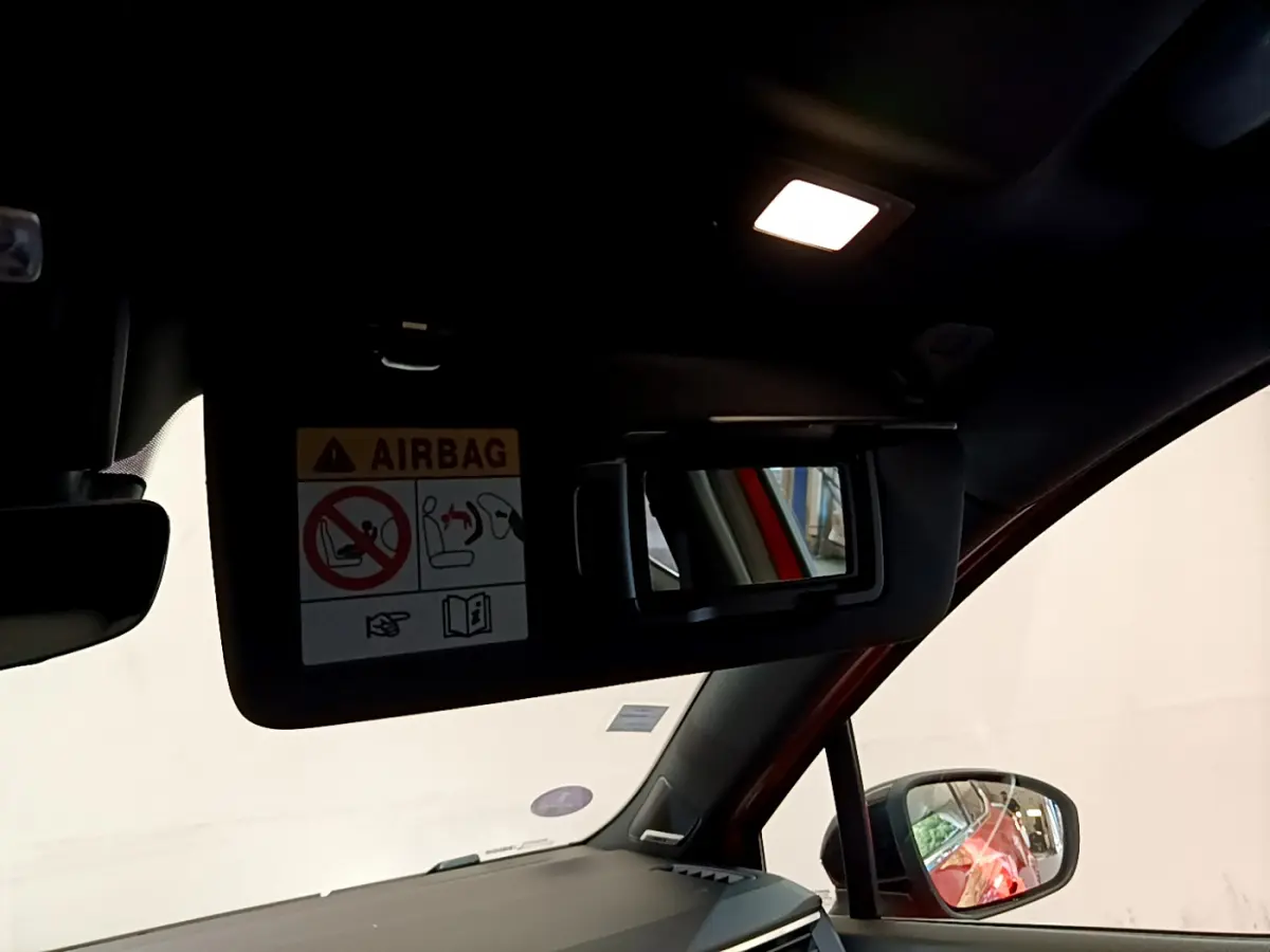 Détail intérieur du pare-soleil côté conducteur avec miroir et avertissement airbag, reflet orange Renault Clio visible au rétroviseur.