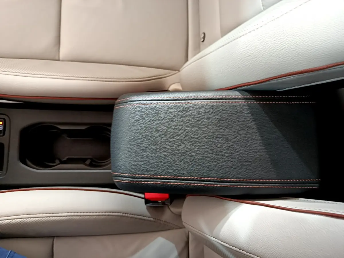 Vue plongeante sur l'accoudoir noir avec surpiqûres orange et sièges cuir beige de la Renault Clio Initiale Paris E-TECH 2021