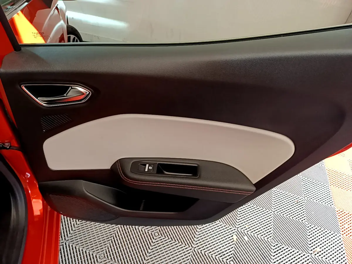 Vue intérieure côté gauche de la porte avant orange de la Renault Clio Initiale Paris E-TECH 140 avec garniture bicolore noire et beige.