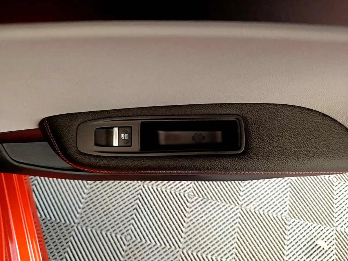 Gros plan sur la poignée intérieure et le bouton de verrouillage de la porte côté gauche d'une Renault Clio Initiale Paris orange.