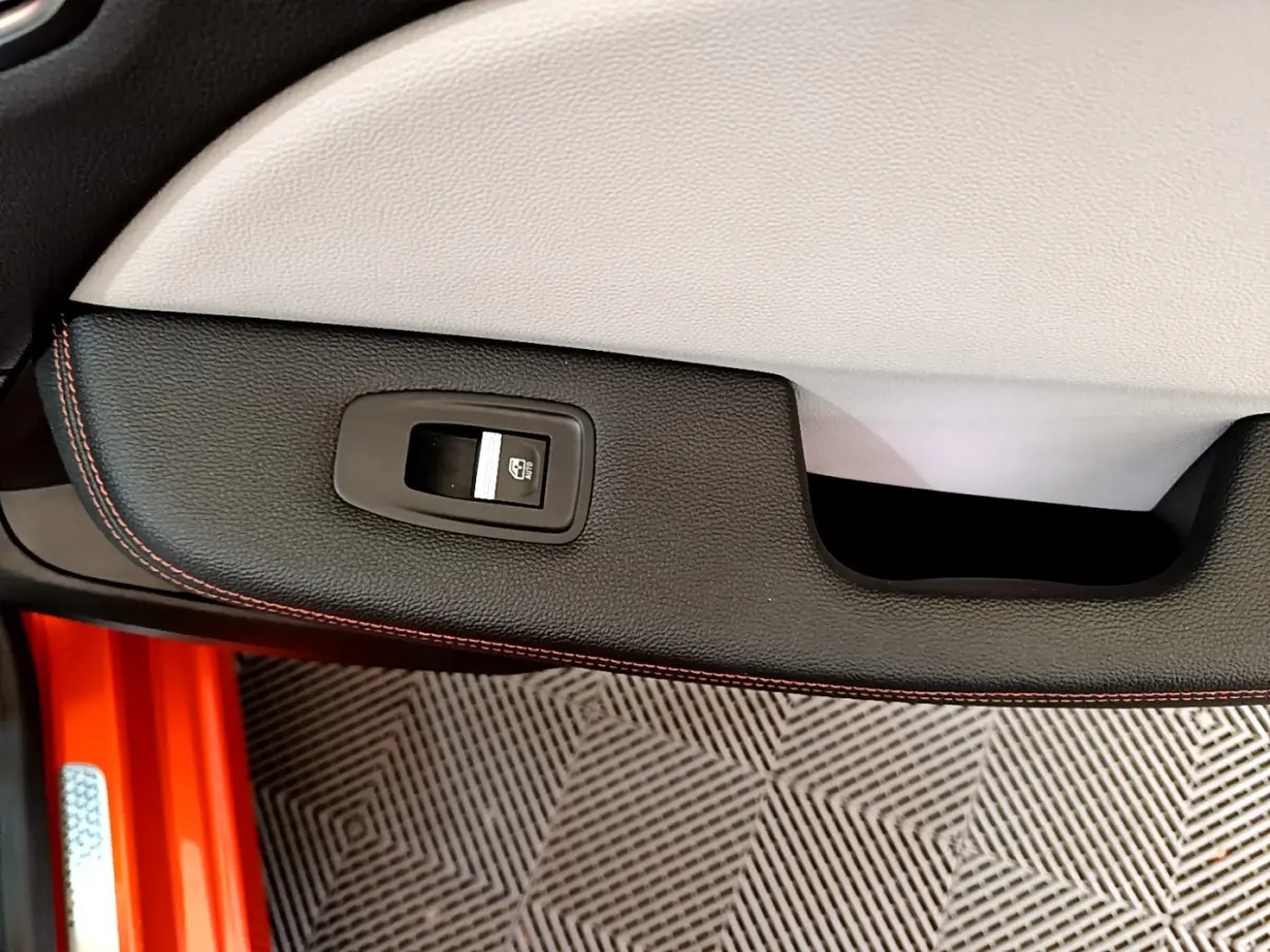 Gros plan sur la commande de lève-vitre côté conducteur, garniture noire avec surpiqûres orange, intérieur Renault Clio orange.