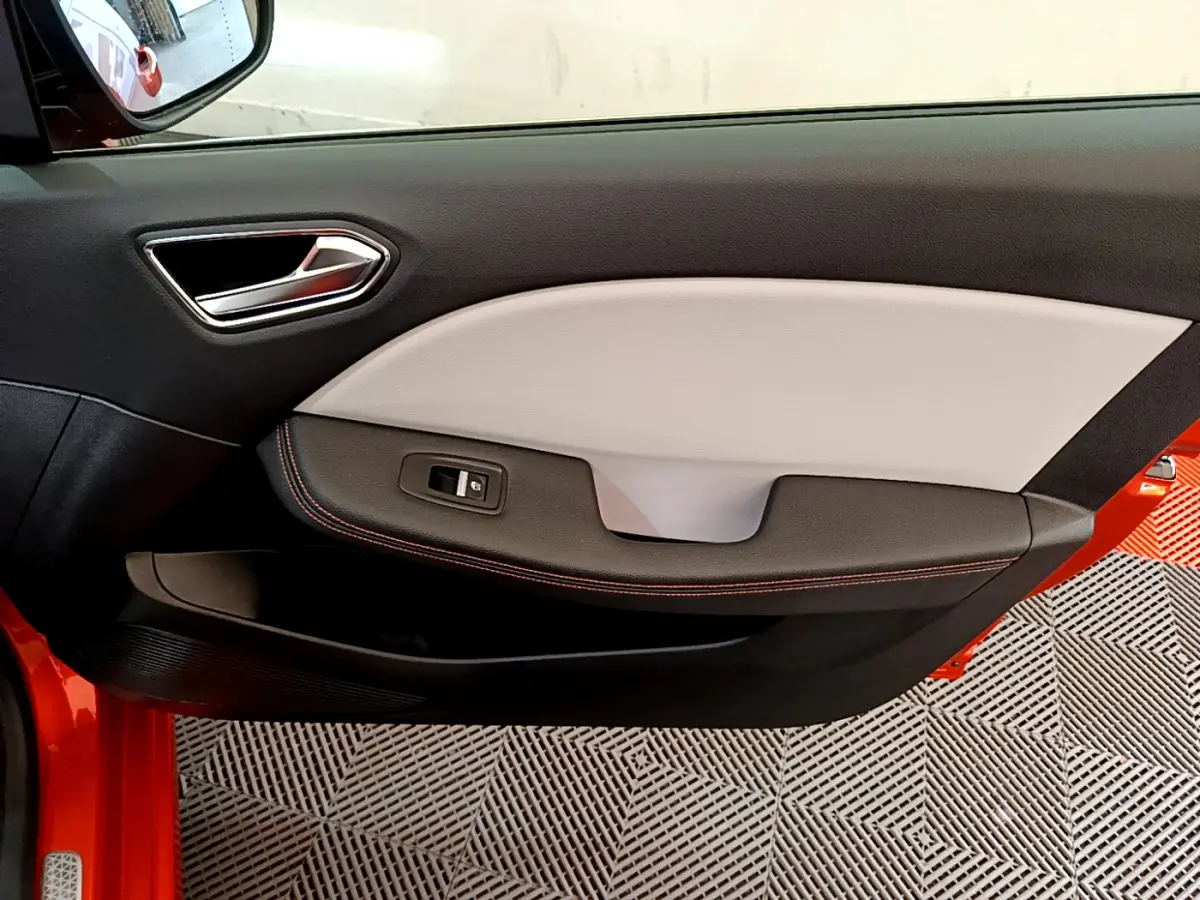 Vue rapprochée de la porte côté conducteur d'une Renault Clio orange 2021, avec garniture bicolore et bouton de vitre électrique.