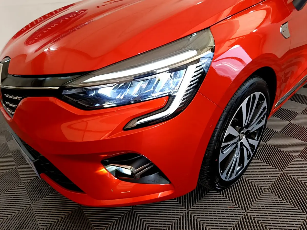 Gros plan sur l'avant droit de la Renault Clio Initiale Paris orange, mettant en valeur le phare LED et la jante alliage.