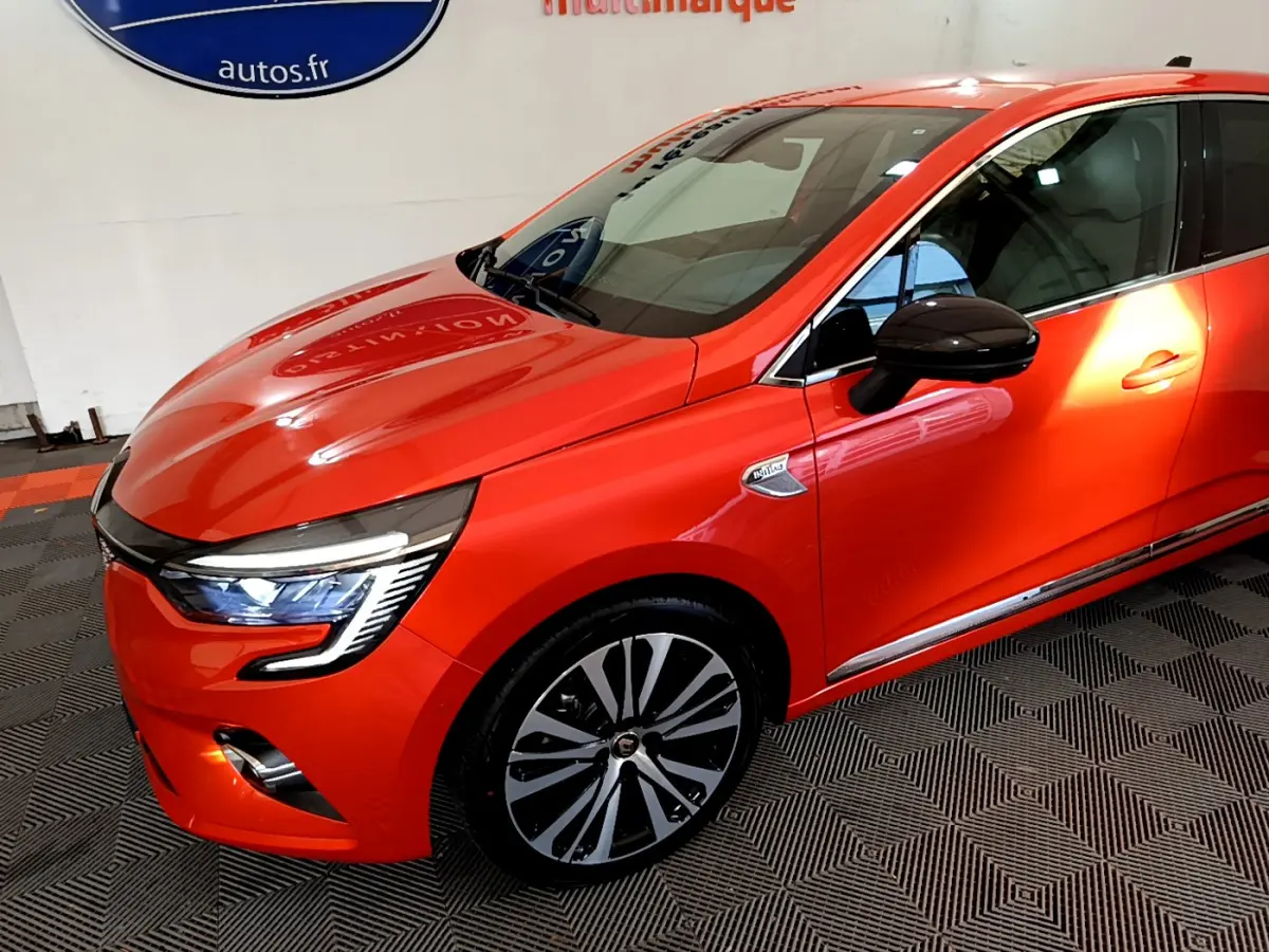 Vue 3/4 avant droite d'une Renault Clio Initiale Paris orange avec phares LED et jantes alliage distinctives.