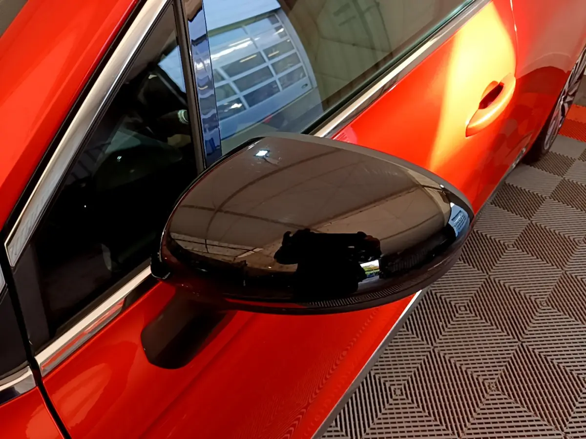 Rétroviseur noir en gros plan côté gauche sur une Renault Clio Initiale Paris orange vue de profil partiel.