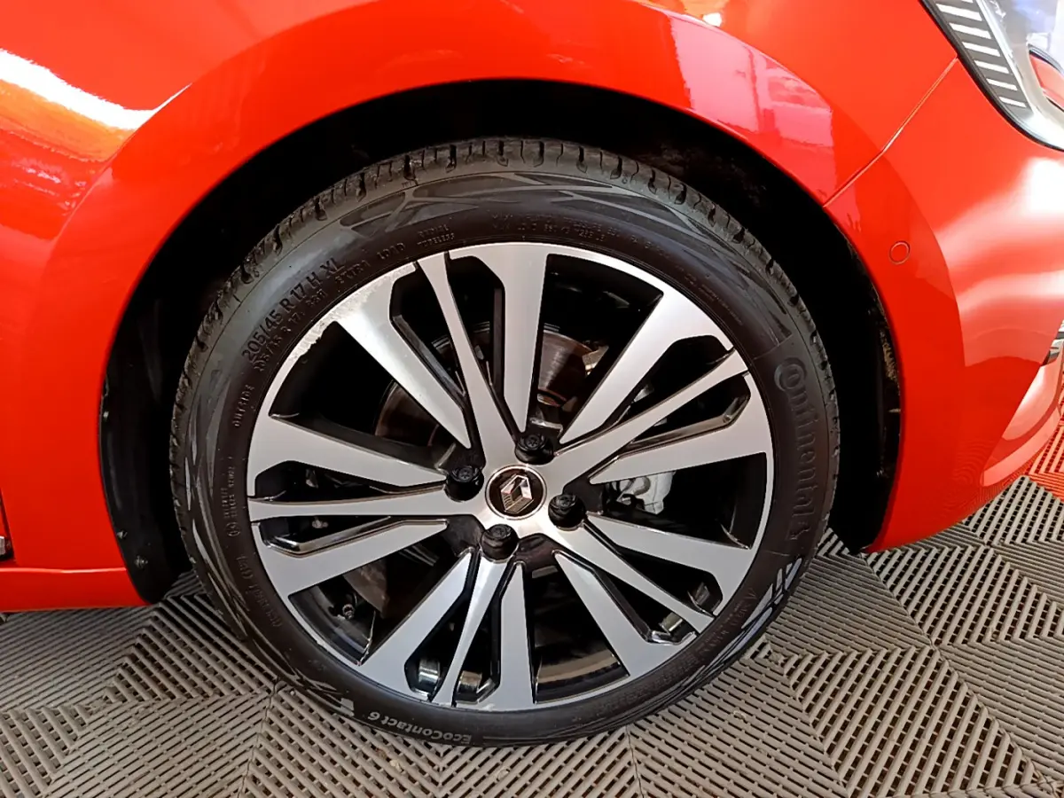 Gros plan sur la roue avant gauche d'une Renault Clio orange 2021 avec jante alliage bicolore et logo Renault au centre.