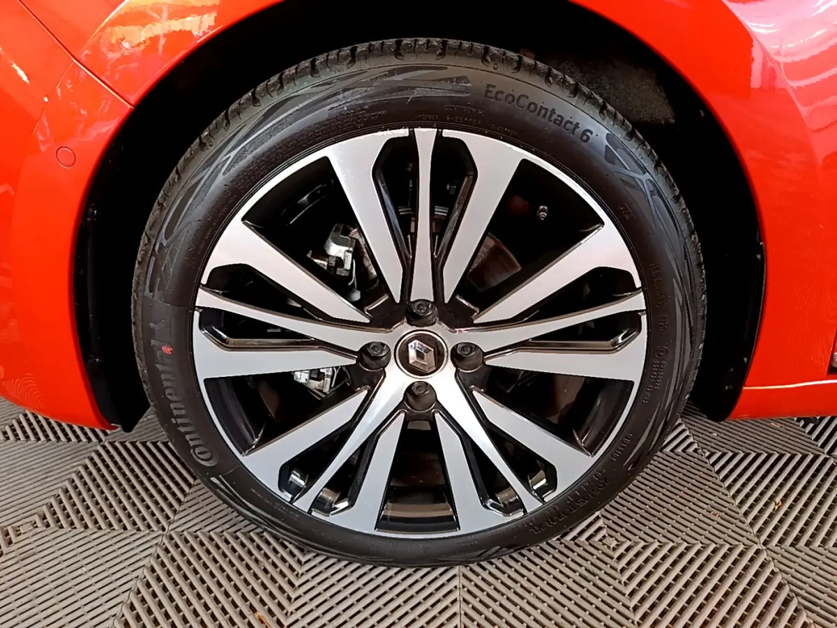 Gros plan sur la roue avant droite de la Renault Clio Initiale Paris orange, mettant en valeur la jante alliage bicolore et le logo Renault.