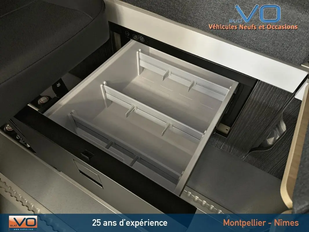 Tiroir de rangement ouvert sous le siège dans l'habitacle du Renault Trafic Fourgon gris 2025, version Confort.