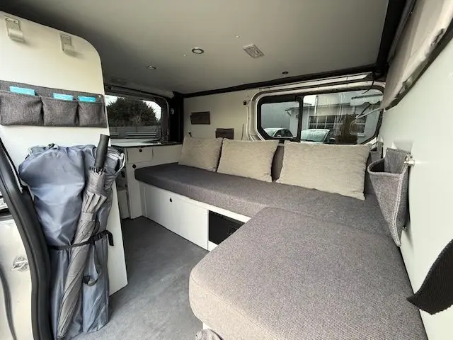 Intérieur du Renault Trafic Fourgon gris platine, vue côté droit montrant banquette avec coussins et rangements muraux.