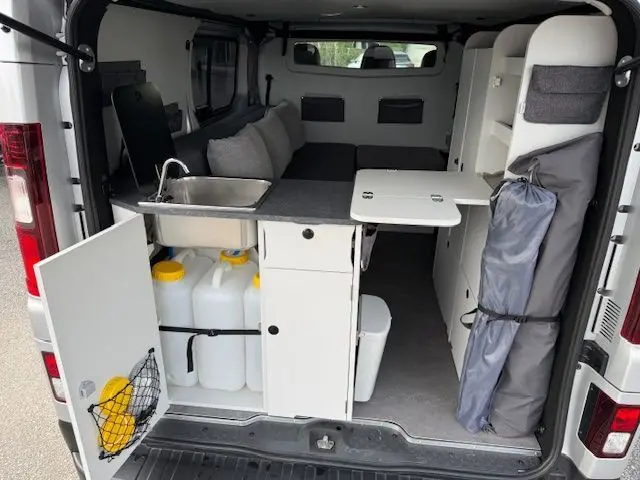Vue arrière intérieure du Renault Trafic Fourgon gris platine aménagé avec kitchenette, rangements et table rabattable.