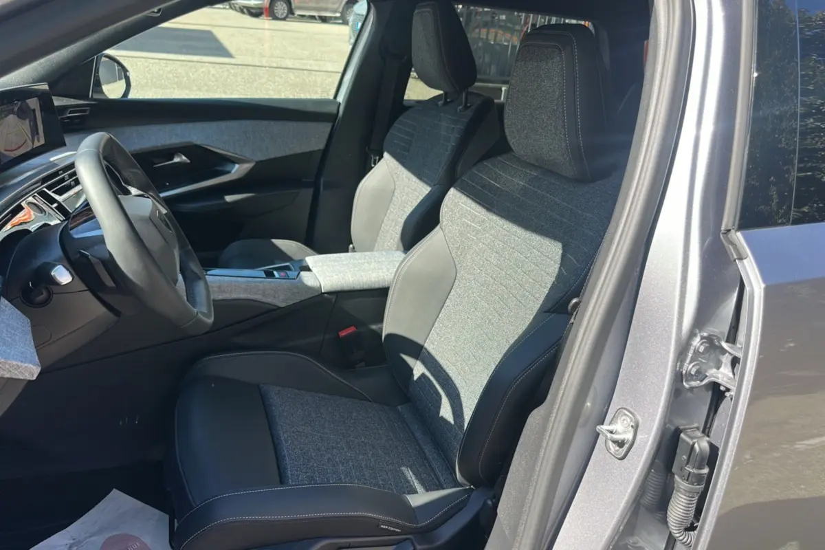Vue intérieure côté conducteur du Peugeot 5008 gris artense, sièges cuir tissu avec accoudoir central et volant multifonctions.