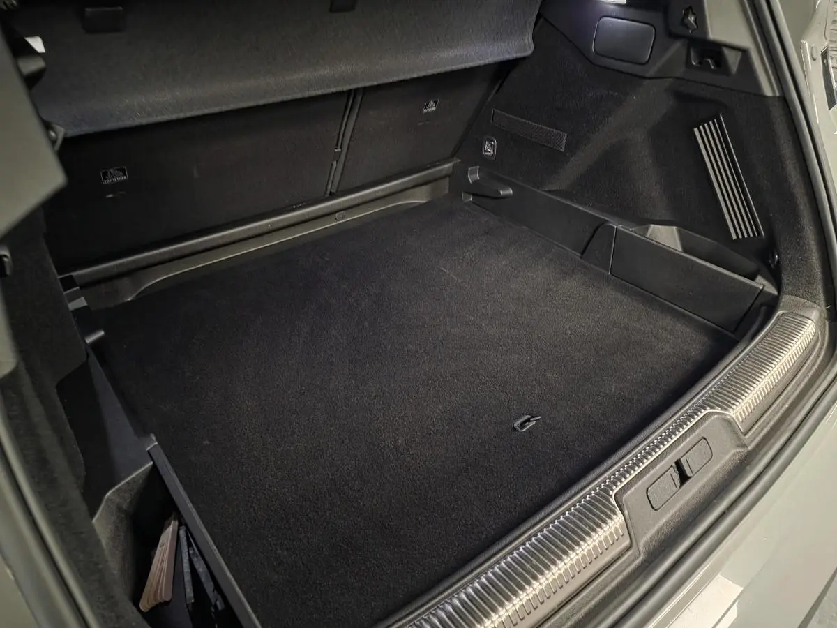 Coffre ouvert du DS7 Crossback gris, montrant le tapis de sol noir et les rangements latéraux.