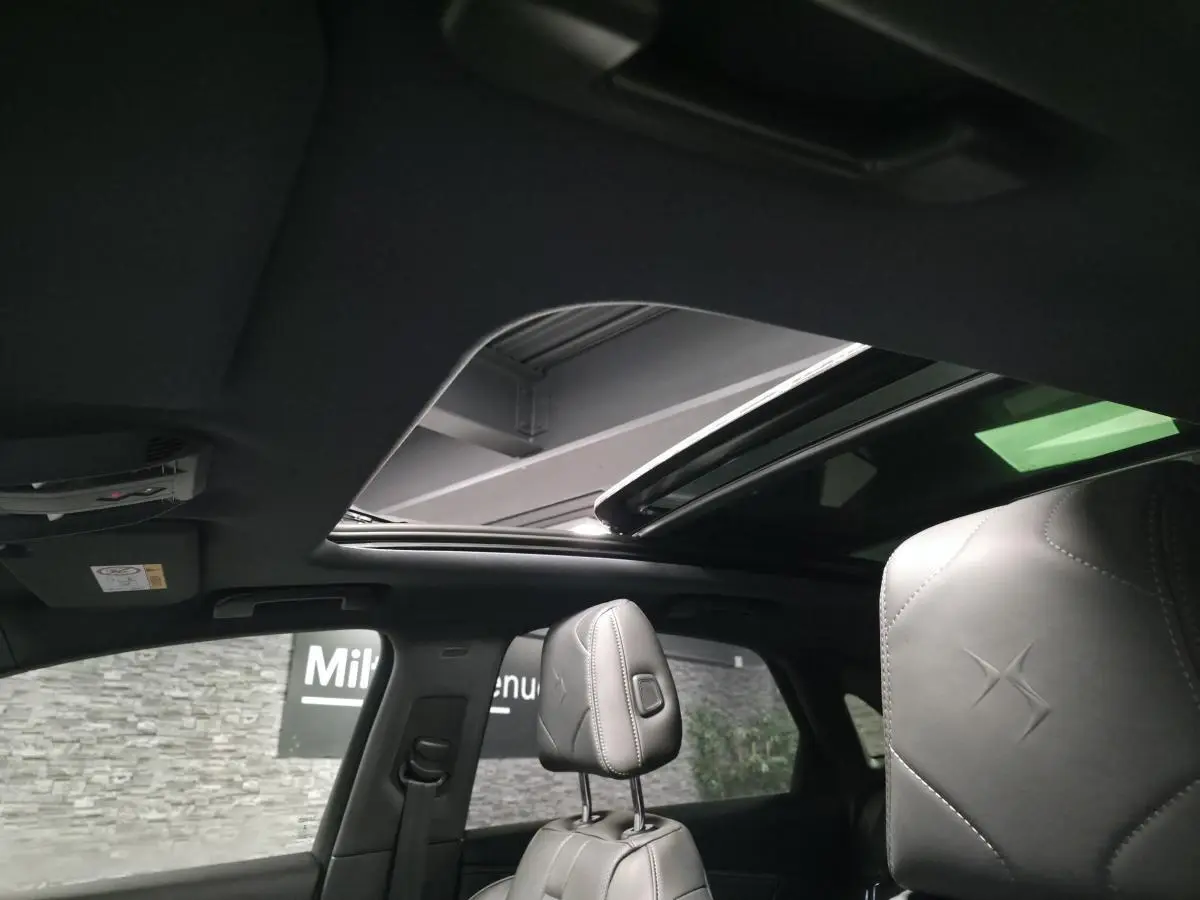 Intérieur du DS7 Crossback gris, vue sur les sièges avant en cuir noir avec toit ouvrant panoramique ouvert.