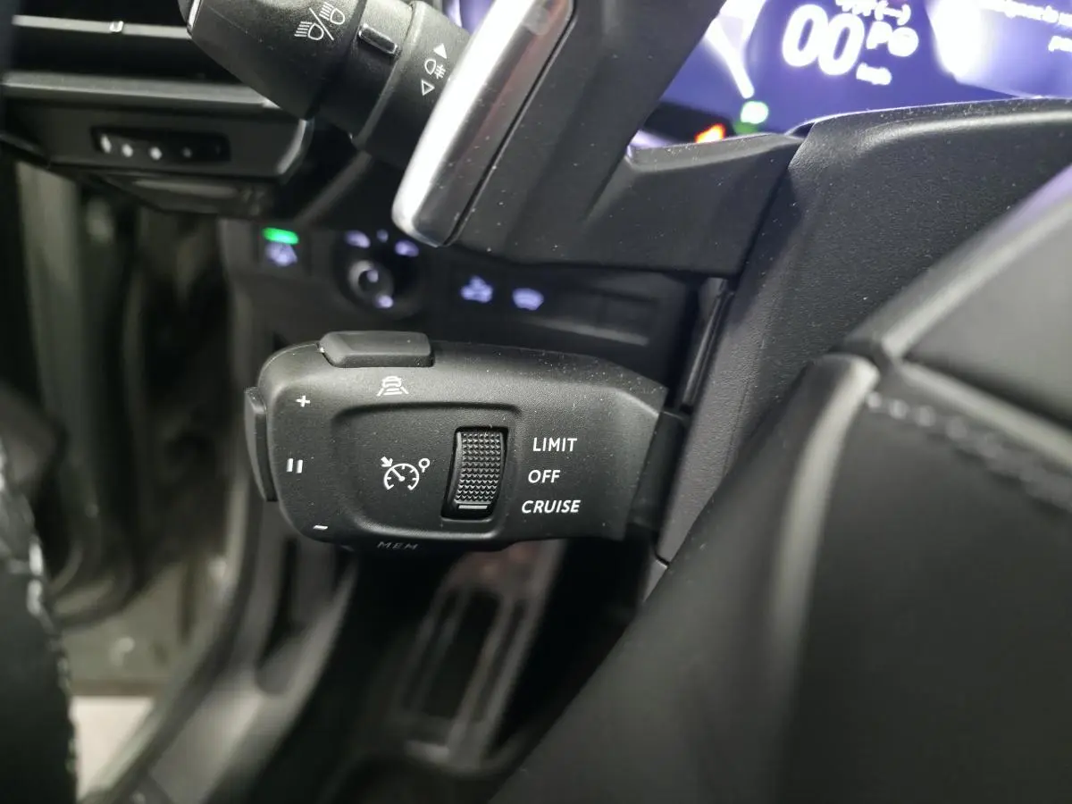 Gros plan sur la commande de régulateur de vitesse au volant du DS7 Crossback gris, avec affichage numérique en arrière-plan.