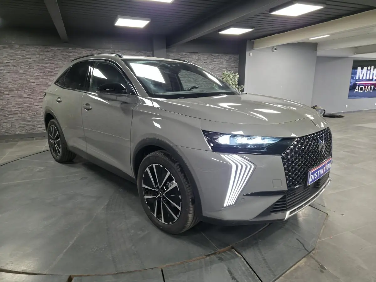 DS7 Crossback gris en 3/4 avant droit, avec calandre noire brillante et feux LED distinctifs allumés.
