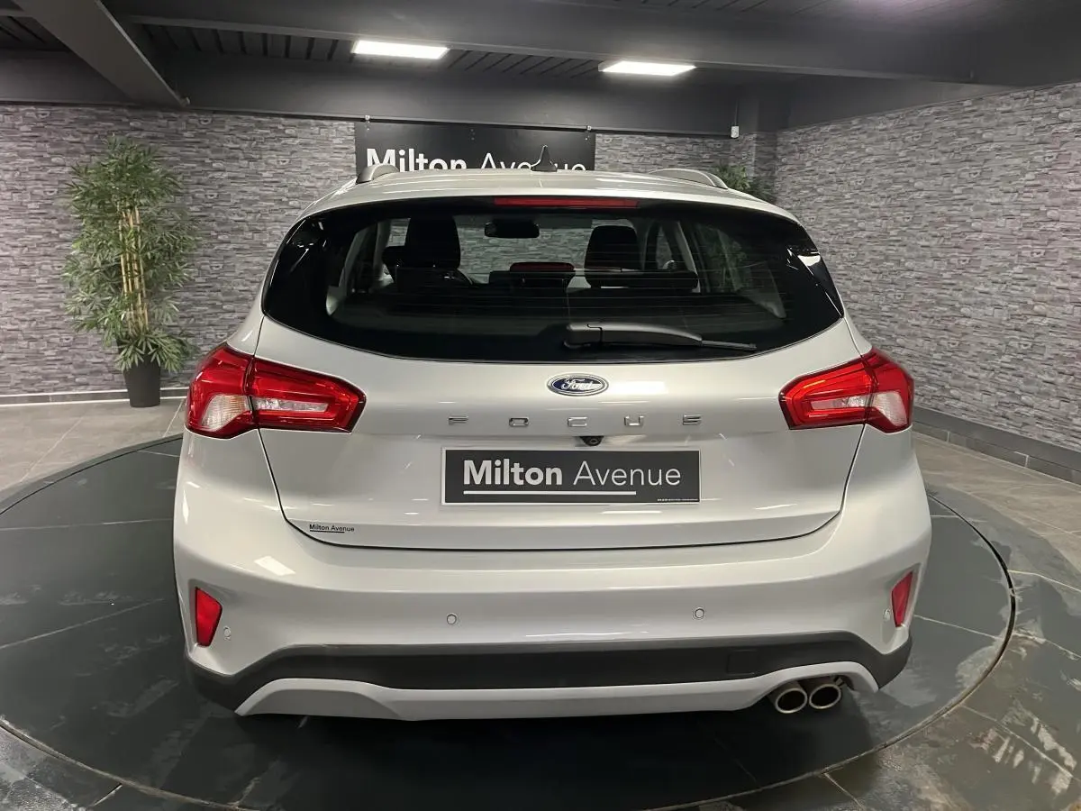 Vue arrière d'une Ford Focus gris clair avec double sortie d'échappement et feux arrière rouges dans un showroom.