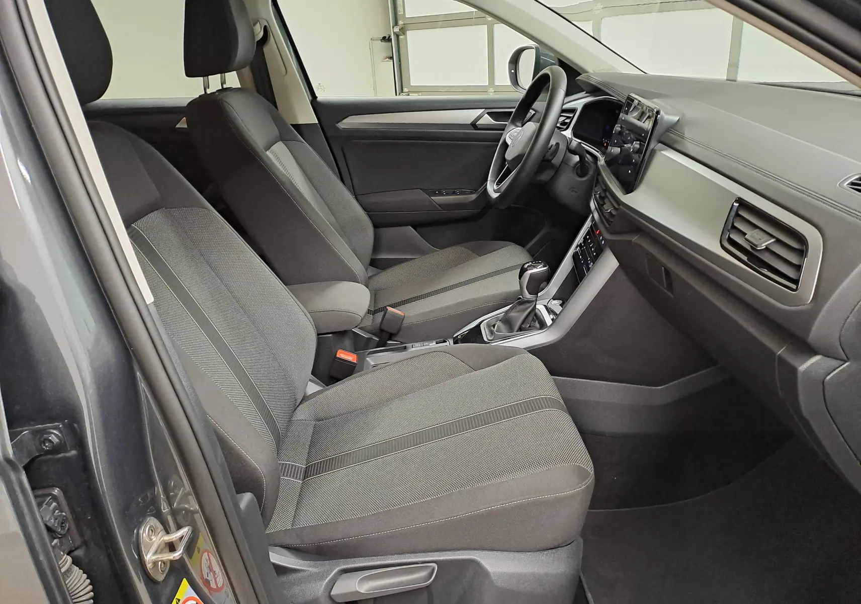 Intérieur avant du Volkswagen T-Roc 2024, sièges tissu gris, tableau de bord moderne avec écran tactile central.