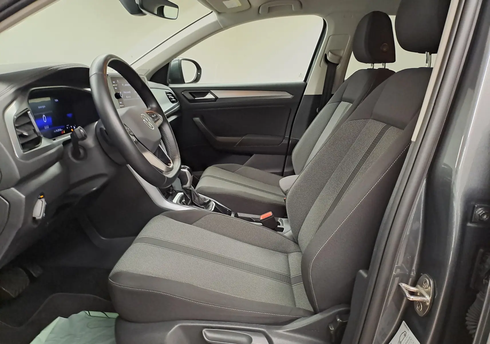 Vue intérieure côté conducteur du Volkswagen T-Roc 2024 gris Indium, sièges tissu et tableau de bord moderne.