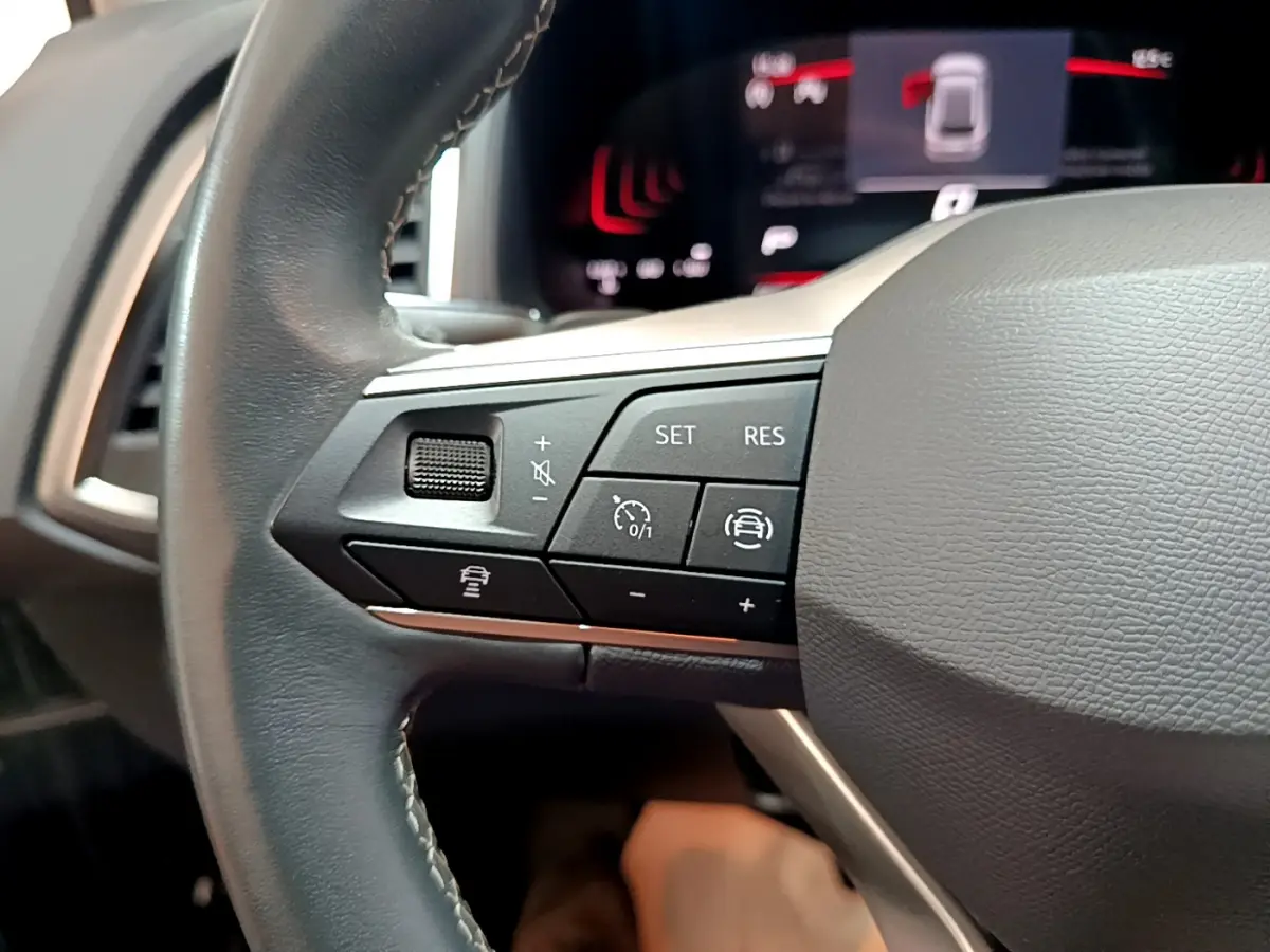 Gros plan sur les commandes du volant côté gauche du SEAT Ateca noir 2022, avec affichage numérique en arrière-plan.