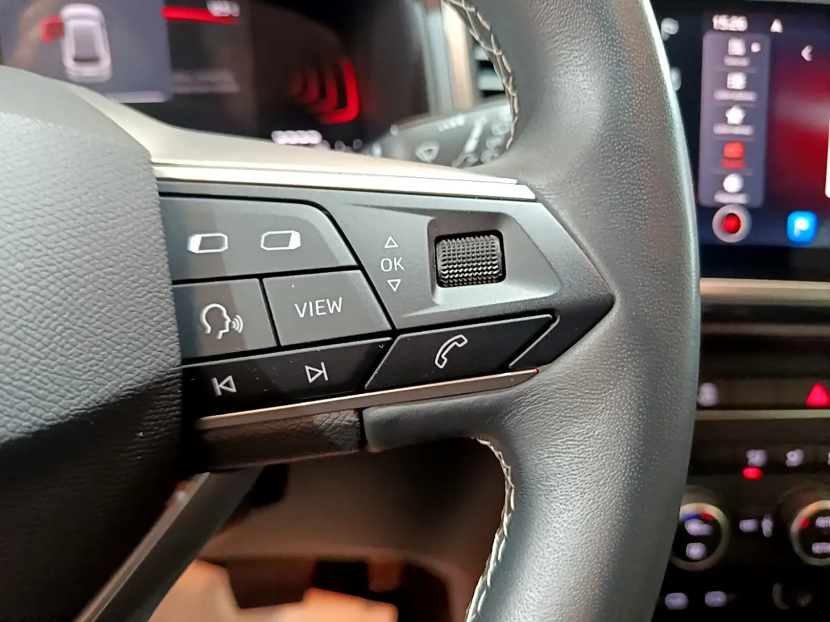 Gros plan sur les commandes du volant cuir noir du SEAT Ateca 2022, avec écran tactile et affichage digital en arrière-plan.