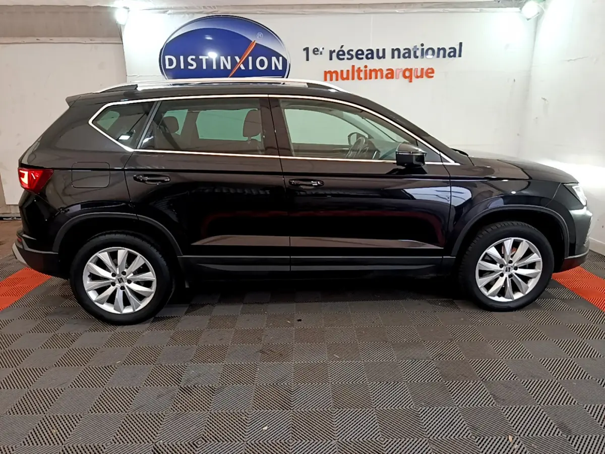 Profil côté droit d'un SUV SEAT Ateca noir 2022 dans un showroom avec jantes alliage et barres de toit chromées.