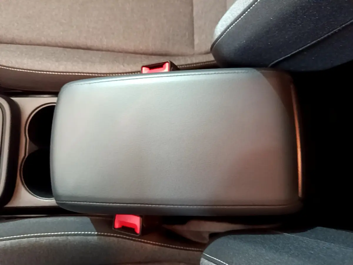 Accoudoir central noir vu de dessus entre sièges avant gris foncé avec ceintures de sécurité rouges visibles