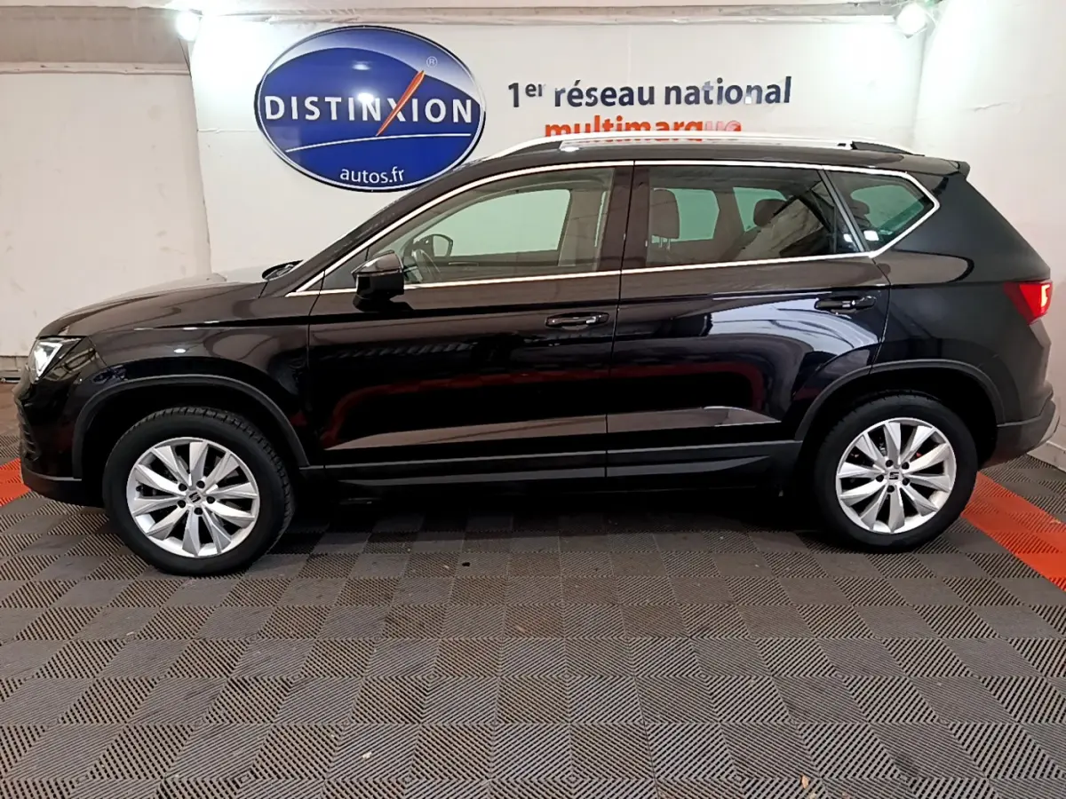 Vue latérale côté gauche d'un SUV SEAT Ateca noir 2022 garé en intérieur avec jantes alliage et barres de toit chromées.