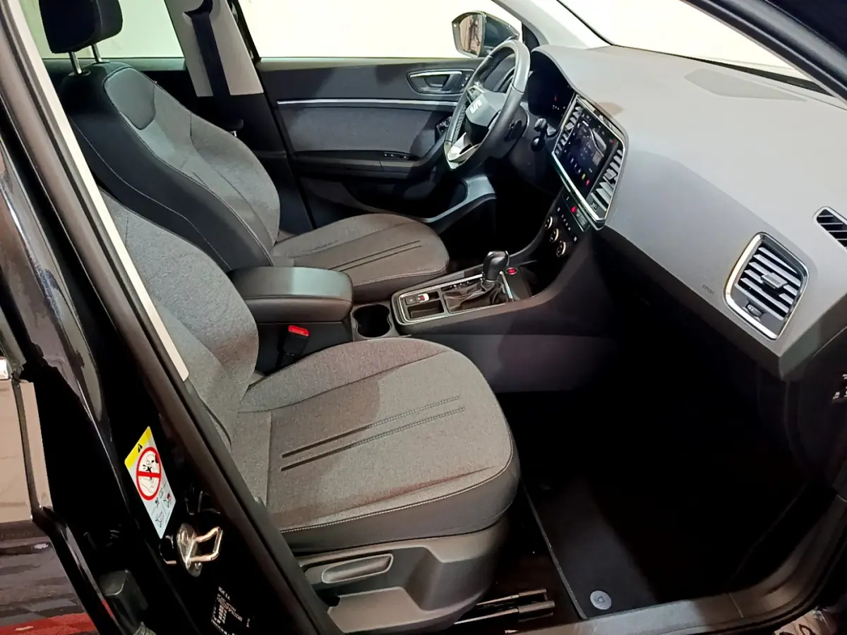 Vue intérieure côté conducteur du SEAT Ateca noir 2022, sièges tissu gris et tableau de bord avec écran tactile.